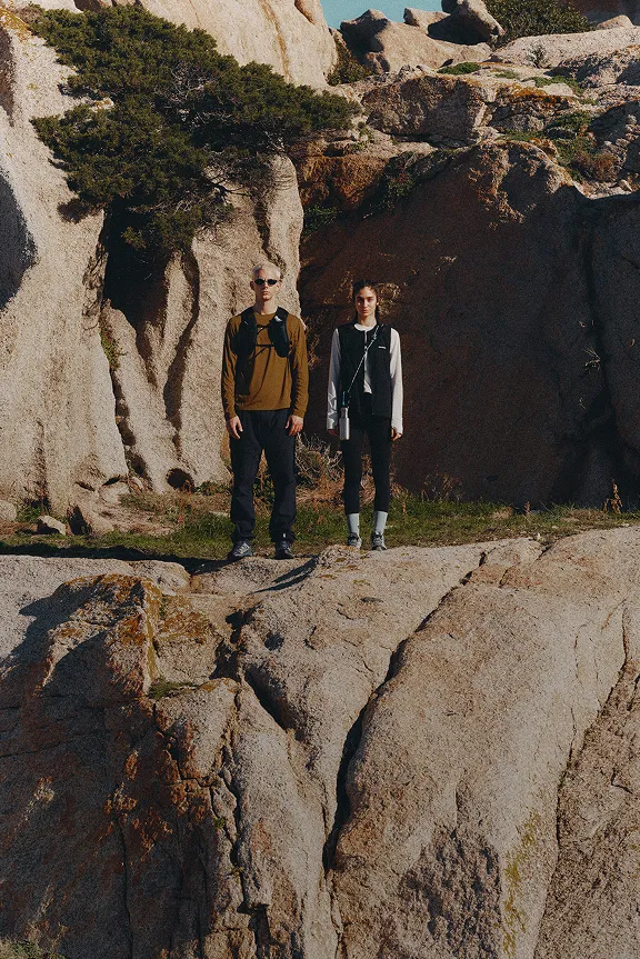 Zwei Wanderer stehen auf großen Felsen in einer felsigen Landschaft unter blauem Himmel.